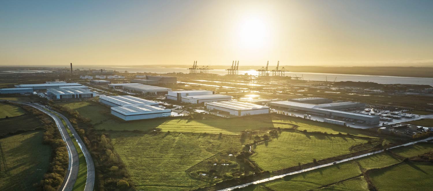 Aerial view of Thames Freeport showing port facilities, warehouses, and cranes near the Thames River at sunset.
